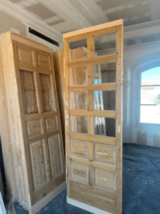 Dos puertas interiores de madera maciza en obra, una con cristales en la parte superior y otra con diseño mixto de madera estilo cuarterones Puerta de madera maciza